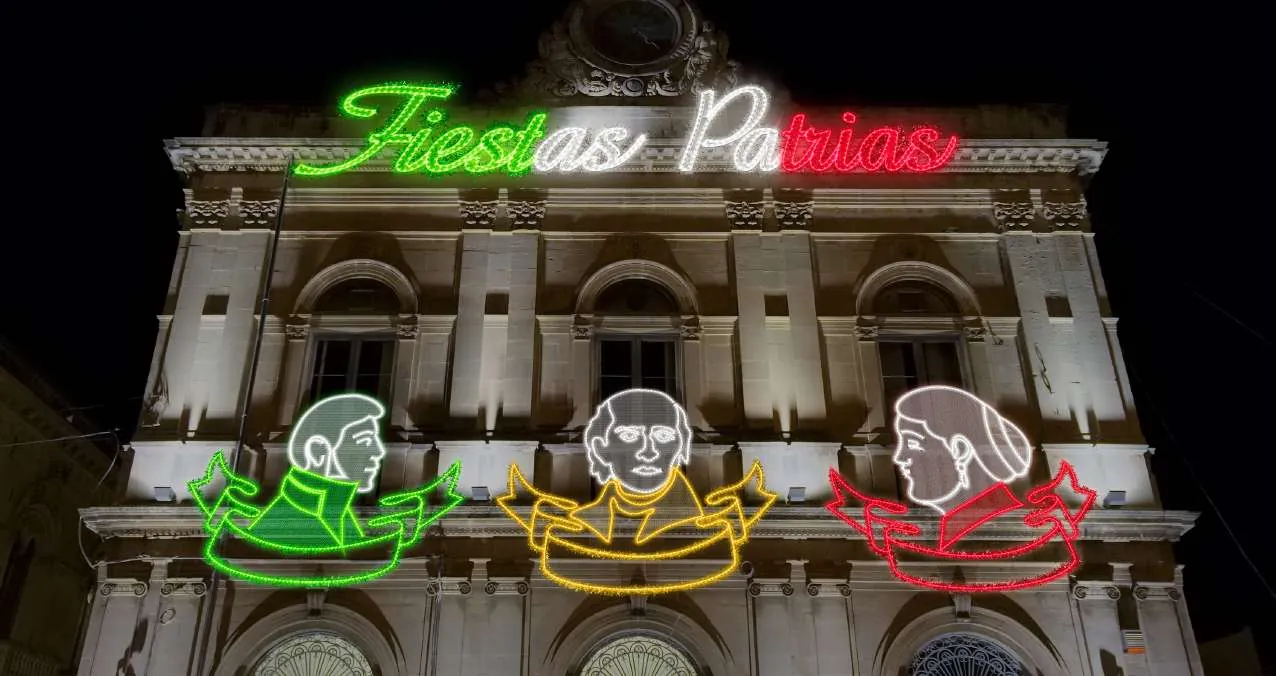 Palacio municipal con letrero 'Fiestas Patrias' y bustos de héroes en luz tricolor
